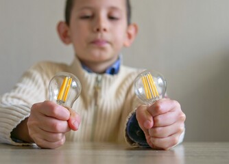 Bright ideas: Conceptual image of a child's hands holding two lightbulbs representing choices and innovation - Young boy holding two efficient LED filament lightbulbs © light