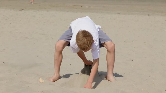 Boy scooping sand with his hands on a sunny beach a vacation by the sea