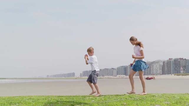 Girl and boy with kites are walking through the green seaweed long distance close-up shot tilt up camera movement