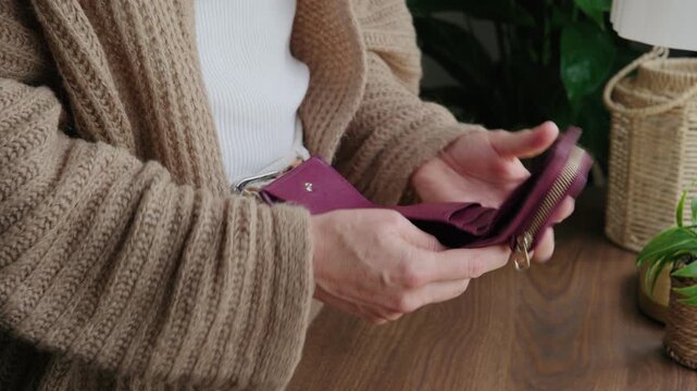 Close-up of a woman opening her wallet, finding no banknotes, and pouring her last few coins into her hand before walking away.