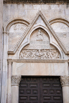 Gothic church portal with carved marble tympanum and relief sculptures in the old town of Cagliari, Sardinia, Italy, ornate medieval stone doorway and dark wooden door, sacred heritage detail