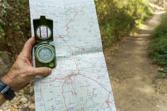 Hiker navigating a wooded trail, holding a compass over a detailed topographic map for orientation and route finding