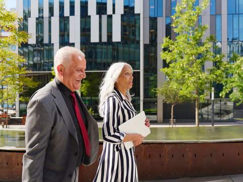 Happy senior businessman walking next to female colleague holding laptop
