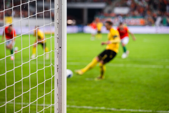 Football goal post and  net with a blurred soccer player in yellow kit shooting a penalty kick