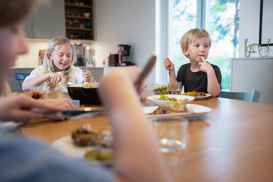 Cute boy with hand on chin looking away during family dinner at home