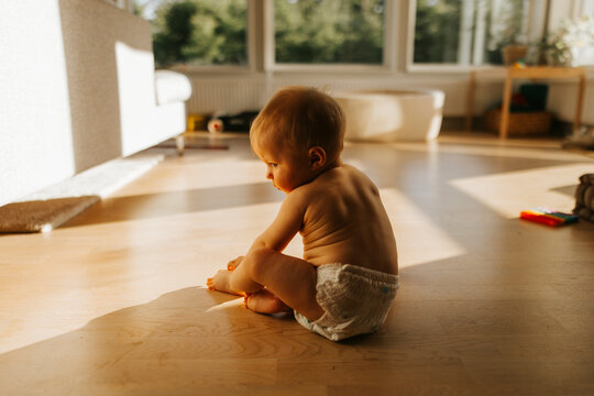 Shirtless toddler wearing diaper sitting on hardwood floor in home