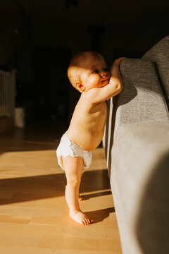 Full length of shirtless infant wearing diaper standing near sofa in home