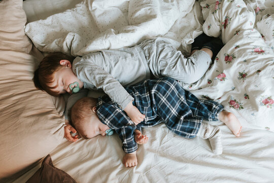 High angle view of brothers sleeping with pacifier on bed in home
