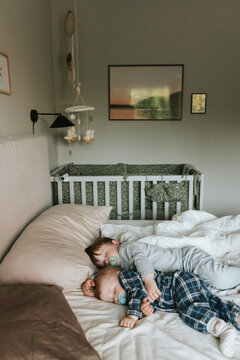 High angle view of male siblings sleeping with pacifier on bed in home