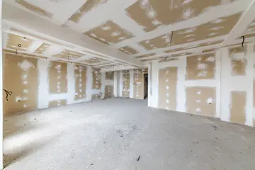 Empty unfinished apartment interior under construction with plasterboard drywall walls, exposed wiring and bare concrete floor, renovation concept © dechevm