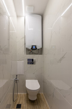 Compact Modern Toilet Room with Wall-Mounted Electric Water Heater. Small Bathroom Interior, Plumbing, Renovation, and Space-Saving Design
