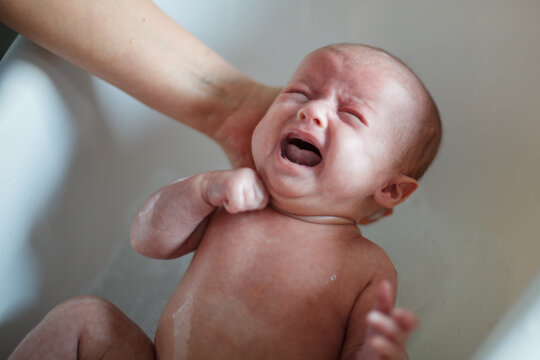 Newborn Baby Crying and Screaming During First Bath in Bathtub Supported by Mother's Hand