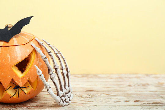 Carved pumpkin, paper bat and skeleton hand for Halloween celebration on light wooden table, closeup