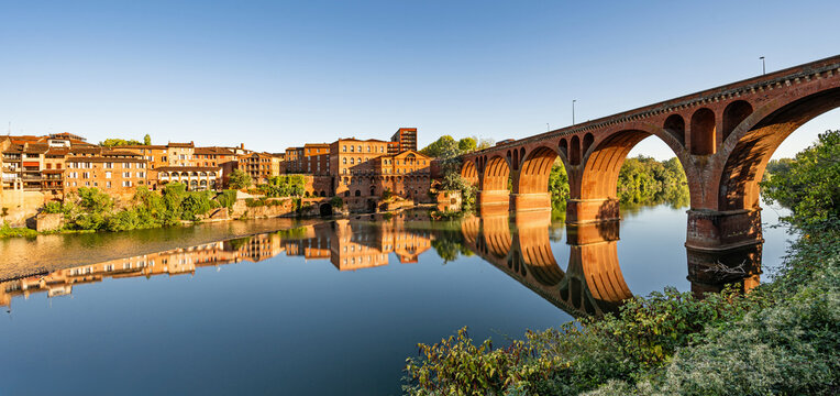 View of the historic old town of Albi as the sun sets, featuring the Pont Neuf (New Bridge, also known as the Bridge of August 22, 1944), which spans the river Tarn.