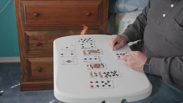 A person sits at a table indoors and places playing cards into rows and piles while setting up a solitaire game.
