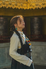 Woman in traditional Tibetan dress with turquoise earring and eyes closed in sunlight, Shangri-La © nhat.photograph
