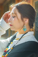 Close-up profile of woman in Tibetan dress with eyes closed and hand raised to her forehead in sunlight, Shangri-La © nhat.photograph