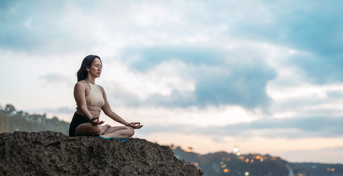 Mindful asian woman meditating and finding inner peace on a quiet beach shore by yoga
