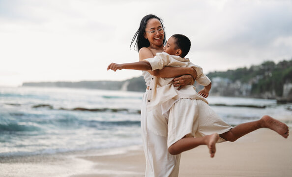 Playful mother spinning her laughing son outdoors during an active beach day