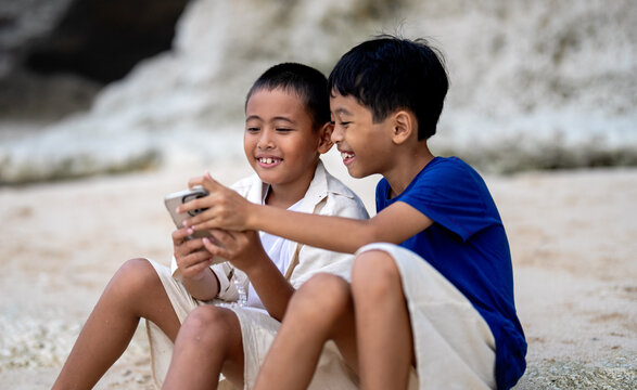 Happy asian brothers playing with smartphone on the beach