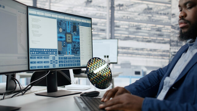 Semiconductor, engineer and circuit design converge as man works at computer beside chip layout software and silicon wafer. Development, research and precision guide technical work in chip facility.