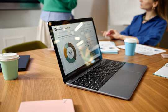 Caucasian woman presenting financial charts with laptop resting on desk during briefing in coworking office. Commercial image suitable for corporate analytics, management, and marketing campaigns