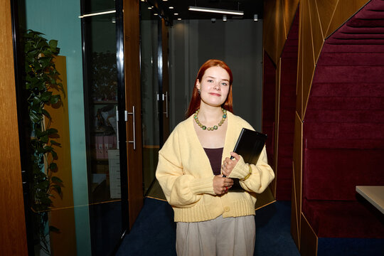 Portrait of young adult Caucasian woman holding digital tablet standing in modern coworking office corridor. Concept representing freelance entrepreneurship and agile corporate workflow