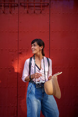 Solo woman traveler carrying a camera and straw hat, exploring a historic city beside a striking red industrial wooden door © Javier Zayaz