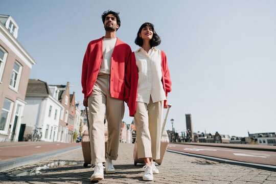 Young couple walking with luggage on a sunny city street for travel banner and urban lifestyle background