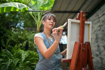 Woman artist painting on canvas at an easel in a lush outdoor garden © Wasana
