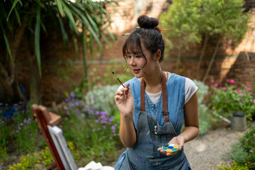 Asian woman artist painting outdoors in a garden © Wasana