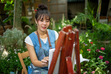 Woman artist painting on canvas at an easel in a garden © Wasana