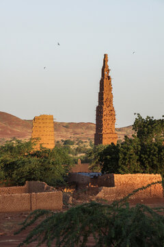 Tall mud minaret of the Bani mosque rising above walls and trees with birds in the sky, Sahel Region, Bani, Burkina Faso