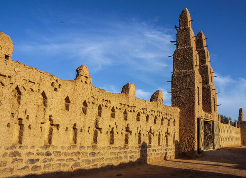 Man in a white robe walking along the decorated mud wall of the Bani mosque near its minarets, Sahel Region, Bani, Burkina Faso