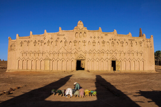 Children praying outside Bani mosque kneeling in a row in front of its decorated facade, Sahel Region, Bani, Burkina Faso