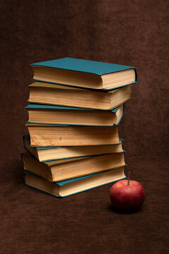 Still life with a stack of books and an apple on a table against a brown background
