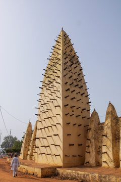 Minaret of the grand mosque with protruding wooden beams and a man walking below, Hauts-Bassins Region, Bobo Dioulasso, Burkina Faso