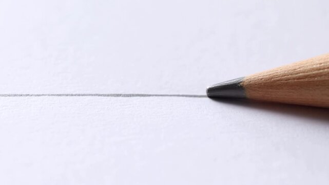 Graphite pencil tip drawing a thin gray line across white paper in closeup