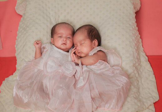 Newborn twin babies resting side by side on a soft cream blanket, sibling bonding, infancy, and newborn care. Wearing delicate white outfits, capturing a tender family moment.