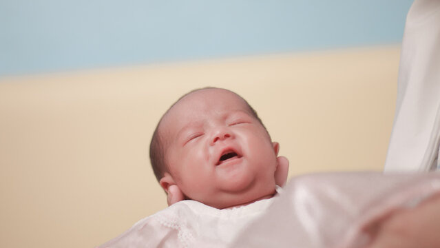 Infant care concepts, newborn, cradle the head, tenderness, and early family bonding. Close up portrait newborn baby gently supported adult hand, wearing white outfit against warm pastel background.
