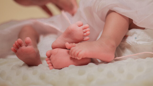 Infant care, feet twin baby, childs, tenderness, family bonding, and early childhood. Close up of newborn baby feet gently supported by an adult hand, with soft natural light and pastel colors.