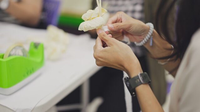 Close-up of a Thai woman making artificial sandalwood paper flowers by hand. Dok Mai Chan is a symbol of mourning and respect used in traditional Buddhist cremation