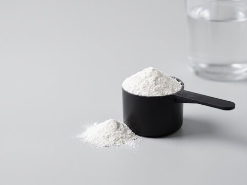 Creatine Monohydrate Powder in Measuring Scoop on Grey Background