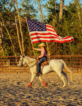 White woman on horseback carrying american flag in outdoor arena