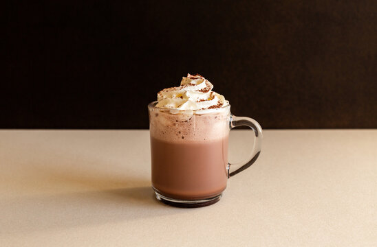 Chocolat chaud avec chantilly et cacao dans une tasse en verre sur fond marron