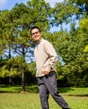A middle-aged Asian man wearing glasses stands in a park.