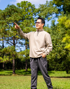 A middle-aged Asian man wearing glasses stands in a park.
