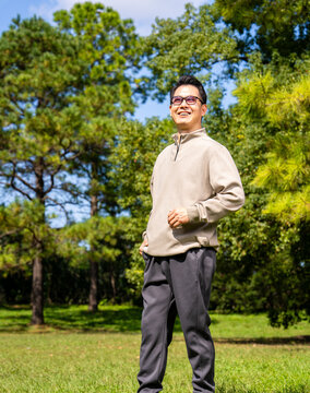 A middle-aged Asian man wearing glasses stands in a park.