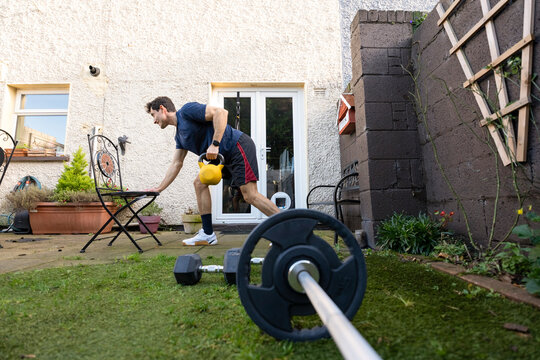 Young Man training in the backyard. Bent-over row with a kettlebell