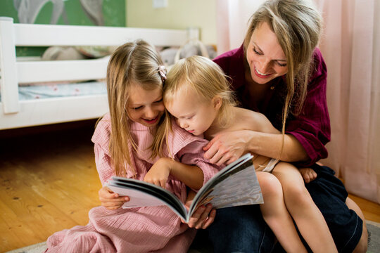 Mother reads picture book with her two daughters on the bedroom floor
